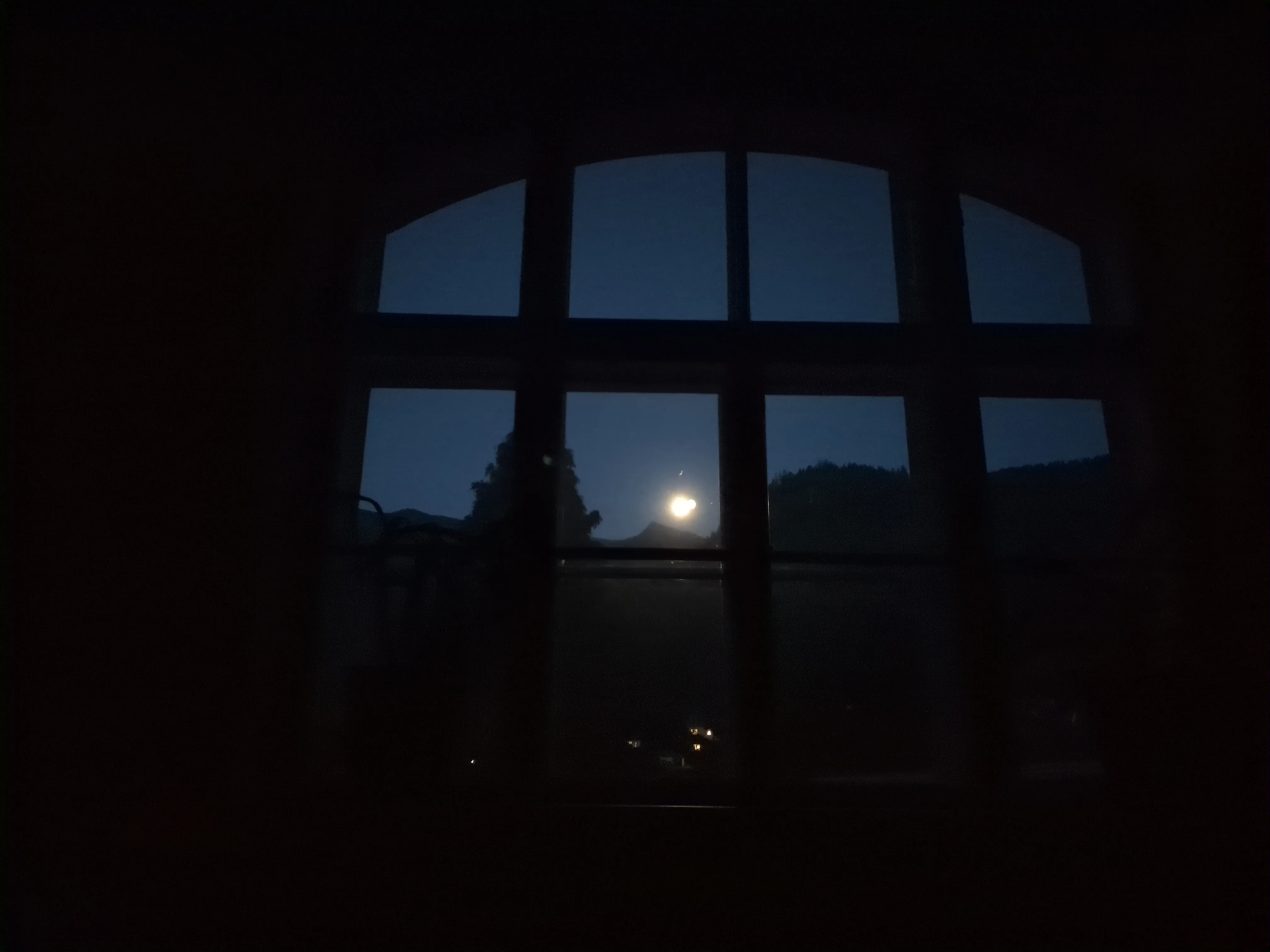 Der Blick durch mein Wiener Kastenfenster (denkmalgeschützter Altbau, eine alte Schule). Es ist Nacht, und über den gegenüberliegenden Bergen ist der Vollmond zu sehen.